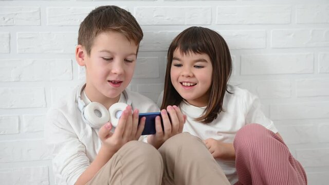 teenager, boy 11 years old with his sister 8 years old emotionally play a blue smartphone, get angry, smile, sit on the floor on a white background at home