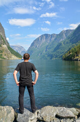 Fototapeta na wymiar Back view of Man looking and enjoying view on the lake and fjords in clear summer day near Naeroyfjord in Gudvangen village, Norway