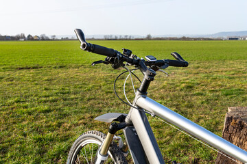 Fototapeta na wymiar A bicycle handlebar seen from the first person perspective. Visible bicycle frame and bicycle accessories on the handlebar and the field in the background.