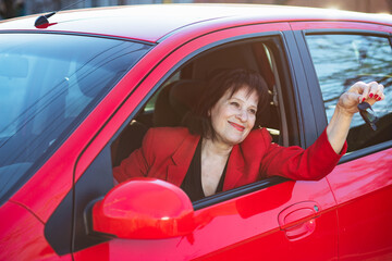 An elderly woman was presented with a red car. Grandma holds keys and smiles