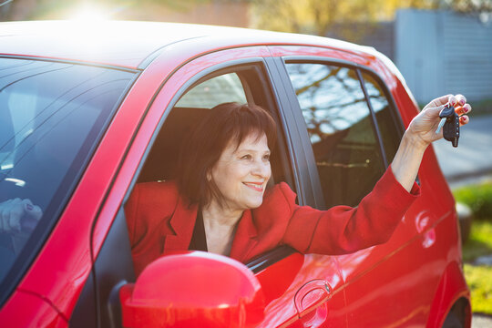 An elderly woman was presented with a red car. Grandma holds keys and smiles