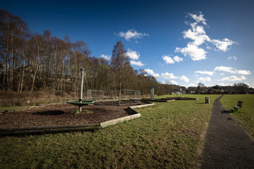 Small rural play park in the middle of a grassy field. Park has a fence around the middle of it,...