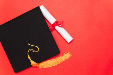 Graduate cap and diploma with red ribbon on red background. Copy space