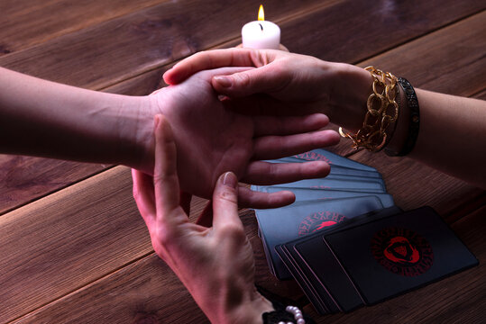 Fortune-teller's hands with prediction cards on a wooden background. The Oracle Visitor draws a card from the divination deck