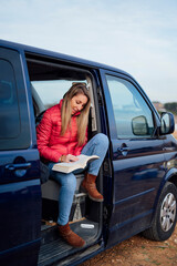 Happy woman reading book on door of camper van