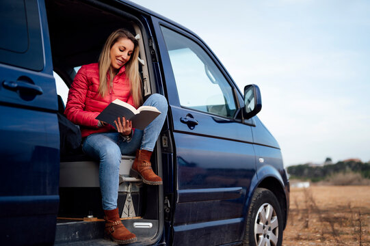 Happy Woman Reading Book On Door Of Camper Van