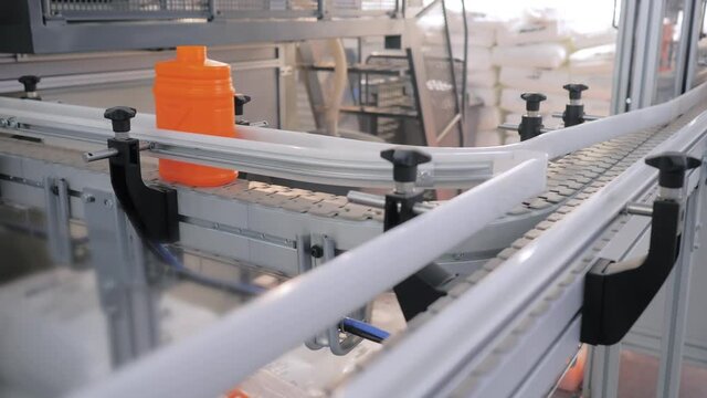 Empty orange plastic jerrycans moving on conveyor belt of automatic pet blow molding machine at factory, exhibition. Manufacturing, recycling, industry, automated technology equipment concept