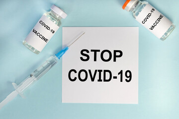 Obraz premium On a blue background among the ampoules and a syringe there is a white sheet on which the inscription stop covid-19. Medical concept. Vaccination of the population