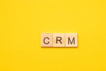Word CRM made from wooden letters on yellow background. Customer Relationship Management