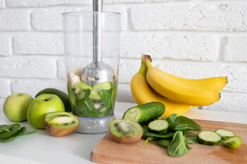 Close-up blender process. Cooking a green healthy smoothie. Mixing in a blender bowl. Making green detox smoothie. Healthy green smoothie with banana, spinach, avocado, apple and mint. Vegan food.