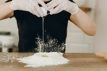 Baker s hands with plain flour well and eggs in preparation process for baking, cooking, pastry...