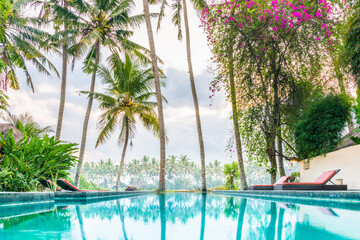 Fototapeta na wymiar Luxury infinity pool and lounge setting in tropical garden landscape with palm trees and rice fields, in Ubud, Bali, Indonesia