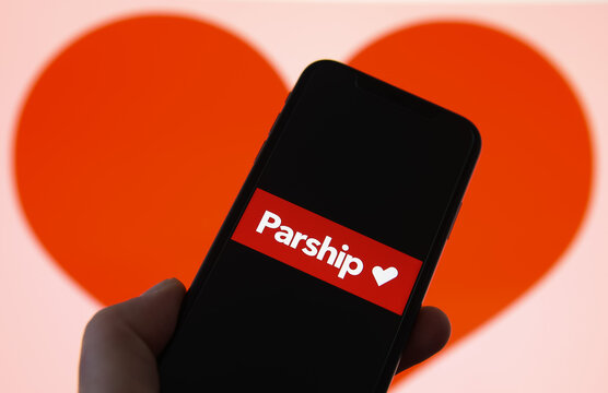 Viersen, Germany - February 9. 2021: Closeup of mobile phone screen with logo lettering of online dating agency app parship, blurred heart background