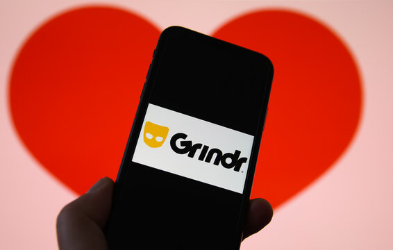 Viersen, Germany - February 9. 2021: Closeup of mobile phone screen with logo lettering of online dating agency app grindr, blurred heart background