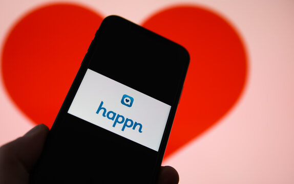Viersen, Germany - February 9. 2021: Closeup of mobile phone screen with logo lettering of online dating agency app happn, blurred heart background