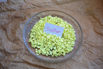 Large yellow granules of sulfur in a round glassware with the name of the substance. 
