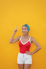 Your text here. I have an idea!Amazed beautiful young woman pointing up while standing against yellow wall.