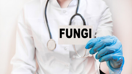 The doctor's blue - gloved hands show the word FUNGI - . a gloved hand on a white background. Medical concept. the medicine