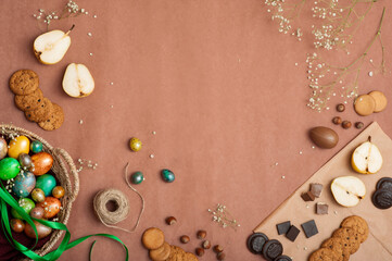 Happy Easter 2021. Colored painted eggs in a wicker basket on a brown background. Easter eggs and sweets. Cookies, pears, and chocolate.