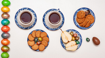 Happy Easter 2021. Colored painted Easter eggs, tea and sweets on a white background. Cookies, pears, and chocolate. Easter board. Tea party. Gzhel painting.