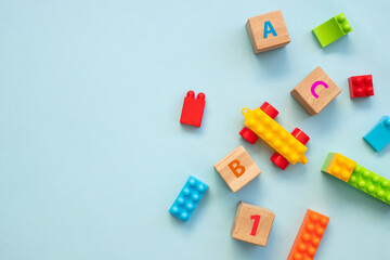Top view of colorful bricks with toys on turquoise wooden table background. Figures and alphabet signs. Education concept