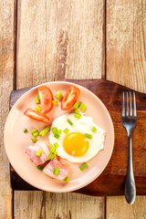 Scrambled eggs with bacon with tomato and onion and on a wooden table in a plate with a fork on a stand.