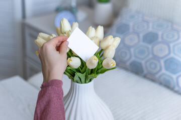 Woman pulling blank greeting card from bouquet of white tulips flowers. Woman day, Copy space. Mock up