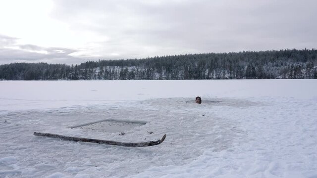 A man swims from one hole cut into the ice to another in a crazy stunt