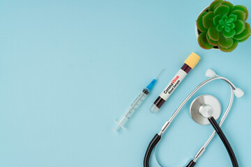 Syringe, stethoscope and blood sample vacuum tube on blue background. Corona virus concept with a copy space.