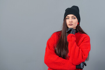 teenage female with a black winter hat and leather gloves, dressed in a red sweater, isolated on gray