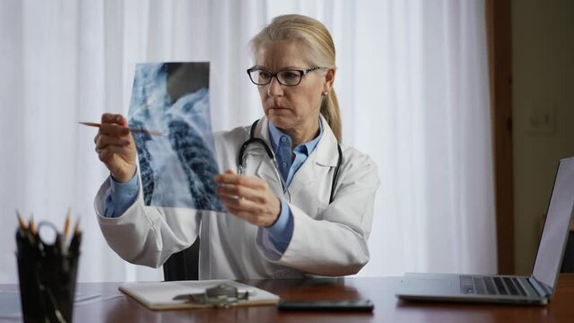 Doctor is looks at X-ray image of patient and reviews information on laptop computer screen. Slow motion concept of doctor for personal healthcare in office.