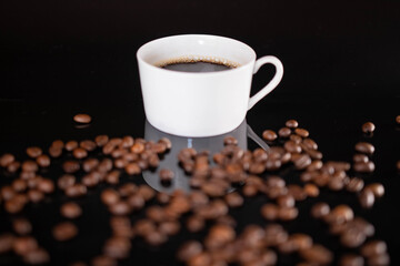Roasted coffee beans and white mug on black background
