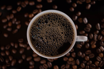 Roasted coffee beans and white mug on black background