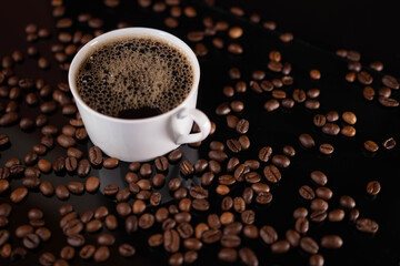 Roasted coffee beans and white mug on black background