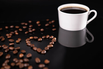 Roasted coffee beans in heart shape and white mug on black background