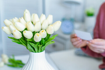 Woman pulling blank greeting card from bouquet of white tulips flowers. Mother day