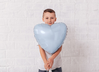 Obraz na płótnie Canvas Boy holds blu heart-shaped balloon on white background