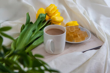 A bouquet of fresh yellow tulips and breakfast with coffee and homemade marmalade. Breakfast in bed. Spring flowers. The concept of spring and holiday, March 8, International Women's Day,