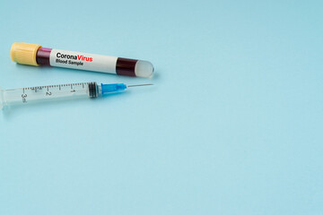 Syringe and blood sample vacuum tube on blue background. Corona virus concept with a copy space.