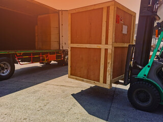 Worker driving forklift loading shipment carton boxes goods on wooden pallet at loading dock from container truck to warehouse cargo storage in freight logistics, transportation industrial, delivery