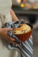 large cupcake in an iron baking dish in female hands on the background of the kitchen.