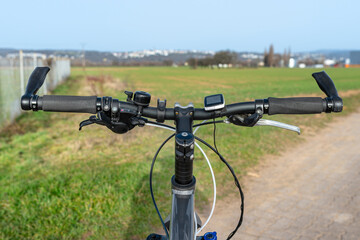 Fototapeta na wymiar Mountain bike handlebar seen from the first person perspective. Visible bicycle frame and bicycle accessories on the handlebar and the field in the background.