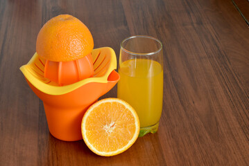 A glass of orange juice, a juicer and half an orange on the table.