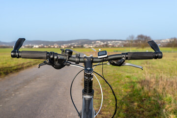 Fototapeta na wymiar Mountain bike handlebar seen from the first person perspective. Visible bicycle frame and bicycle accessories on the handlebar, and the road in the background.