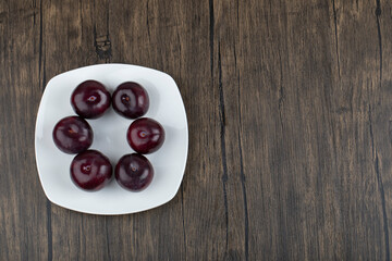 A white plate of fresh delicious plums on wooden table