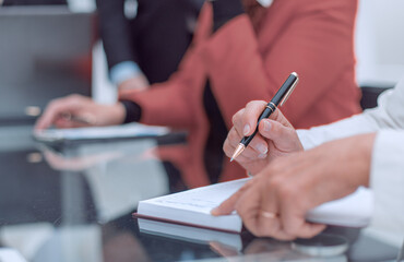 Close up female hands with pen writing on notebook at the meetin
