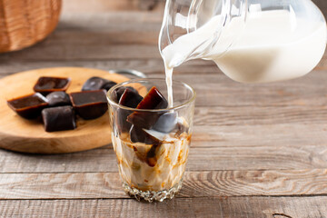 Pouring milk into a glass of ice cube frozen Americano on a table