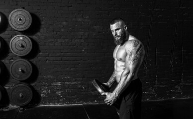 Young active sweaty strong muscular fit man with big muscles holding heavy barbell weight plate in...