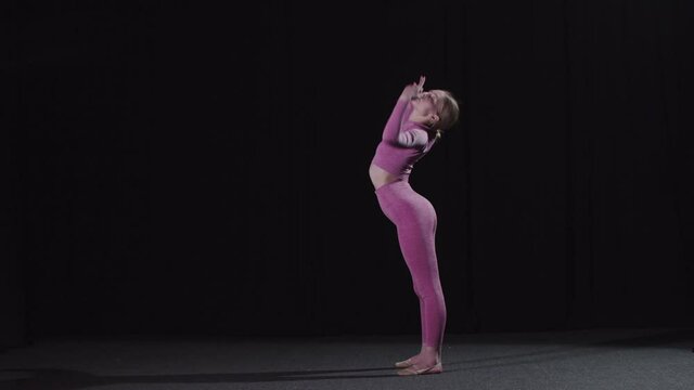 Young female gymnast stands in a bridge pose and moving her leg up