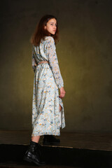 Fototapeta premium model girl in long printed dress and black boots full body portrait walking on dark wall background